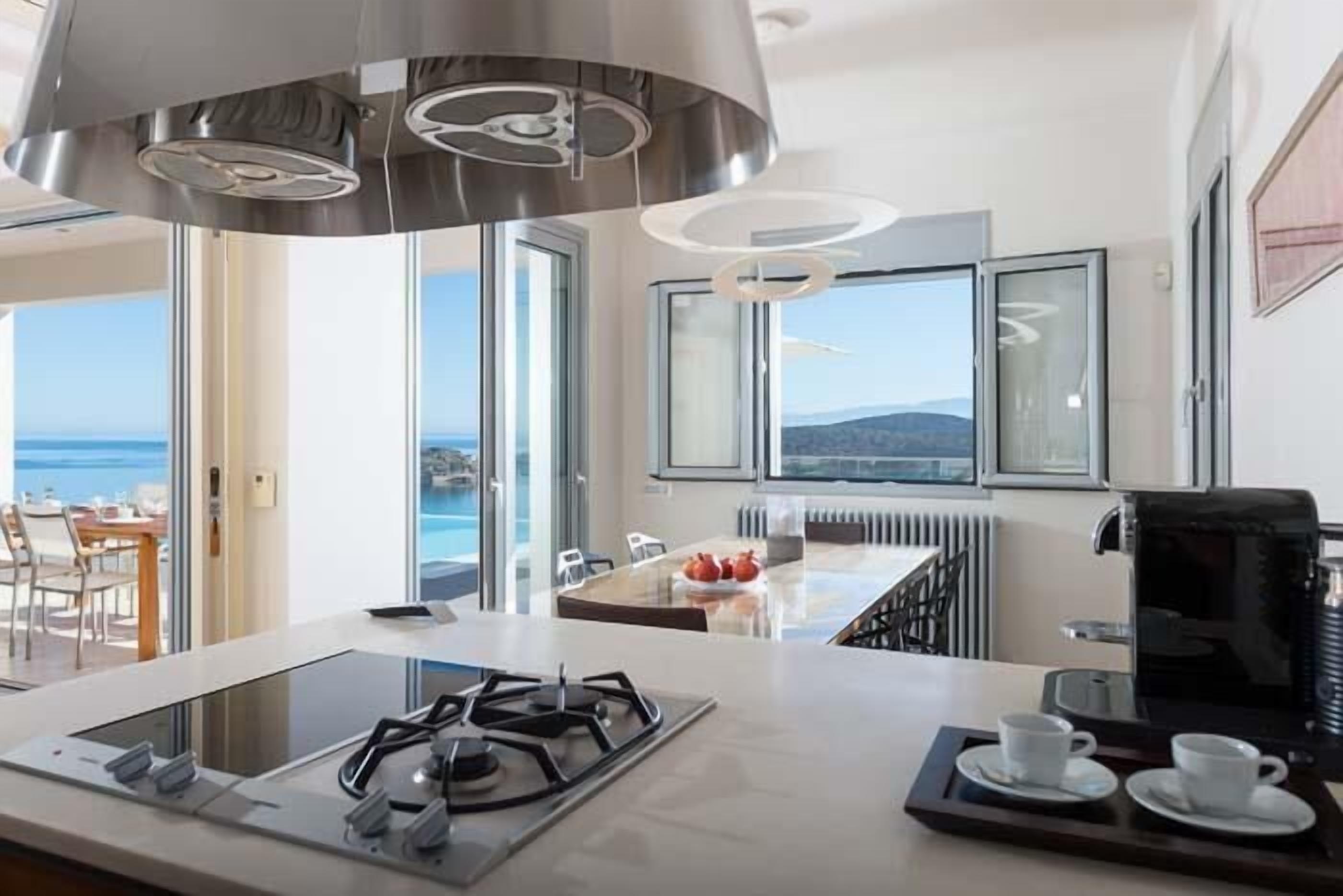 A modern kitchen with a gas stove, a coffee machine, and a view of the sea through large windows.