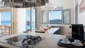 Una cocina moderna con estufa a gas, cafetera y vistas al mar a través de amplios ventanales.