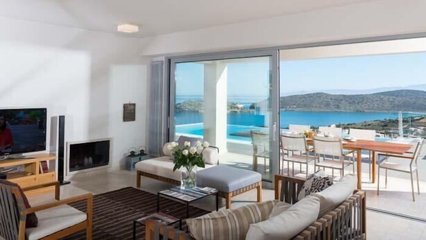 A modern living room with a television, seating, and a large window overlooking a scenic coastal view.