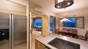 A modern kitchen with a built-in stove, stainless steel appliances, and a view of the ocean through the dining area. - Sea view 3 bedroom villa close to Plaka beach (Elounda)