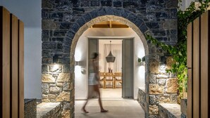 An arched stone entrance leading to a room with a dining area, a hanging light fixture, and a plant on the right. - Villa Anemos Heated pool (Agios Nikolaos)