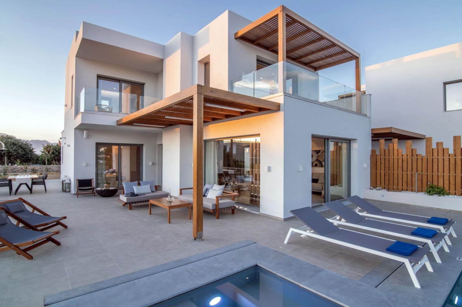 Een modern huis met twee verdiepingen, een overdekte buitenzitplaats, een zwembad en een houten omheining.
