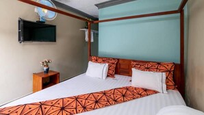 A hotel room with a bed, a small wooden nightstand with a vase of flowers, a wall-mounted TV, and a ceiling fan. - Haber Motel  (Entebbe)