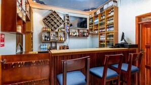 A bar area with wooden shelves stocked with bottles, a counter, and three bar stools. - Haber Motel  (Entebbe)