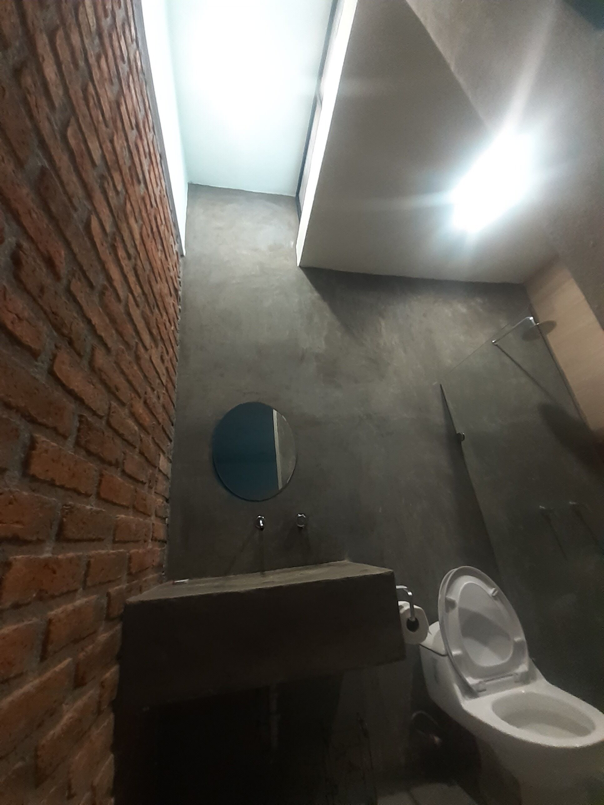 A bathroom with a brick wall, a round mirror, a toilet, and a sink.