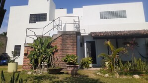 A modern white building with a brick entrance, surrounded by various potted plants and a clear blue sky. - Bungalow loft with large garden and rural area close to all amenities (Puerto Vallarta)