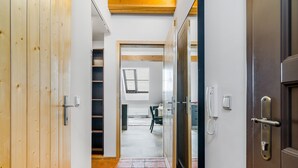A hallway with a wooden door on the left, a glass door on the right, and a tiled floor. There is a small window with blinds in the background.