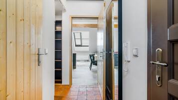 A hallway with a wooden door on the left, a glass door on the right, and a tiled floor. There is a small window with blinds in the background.