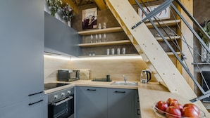 A modern kitchen with grey cabinets, a built-in oven, a coffee machine, and a wooden staircase.
