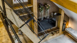A staircase with a wooden finish, a fireplace with a black screen, and two vases with dried flowers.