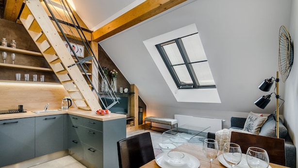 A modern kitchen with a wooden staircase, a dining area with a table set for four, and a large skylight.