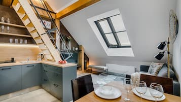 A modern kitchen with a wooden staircase, a dining area with a table set for four, and a large skylight.