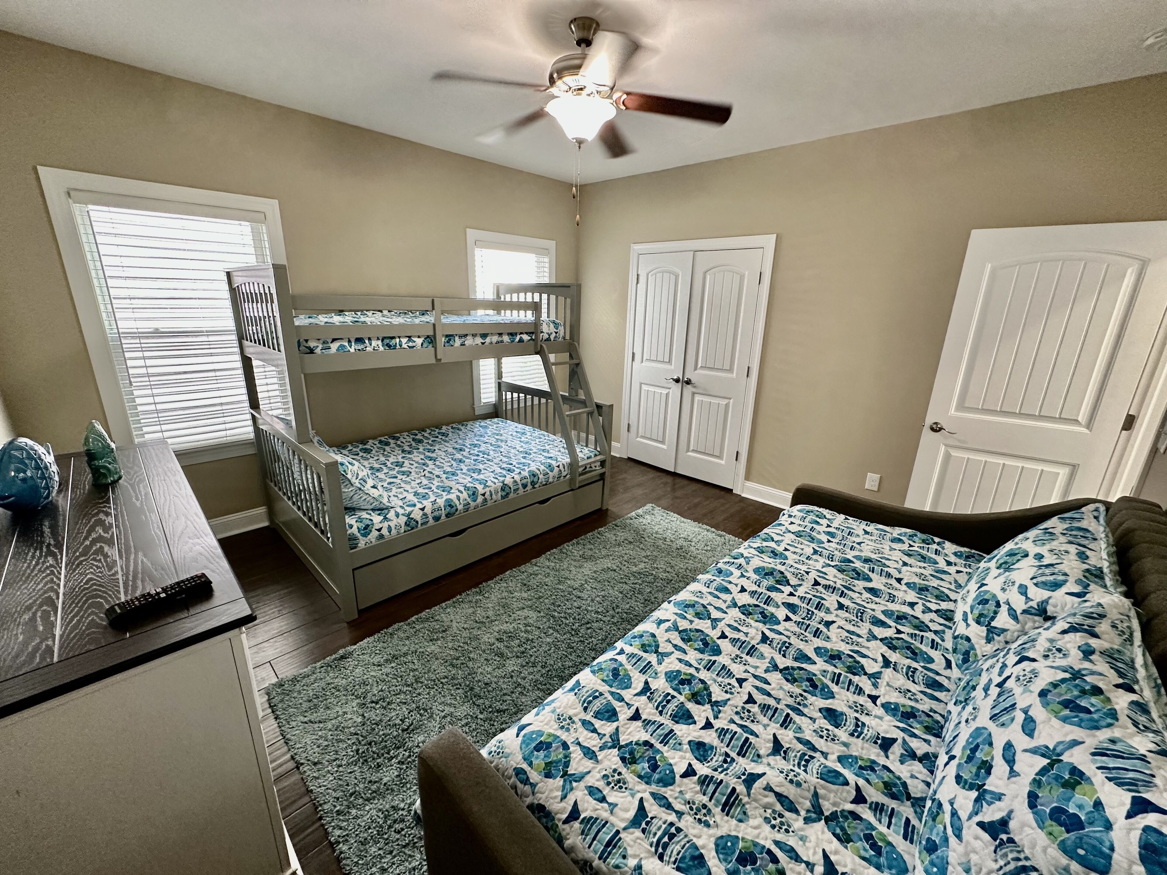 A bedroom with bunk beds, a desk, a bed with a patterned bedspread, and a ceiling fan.