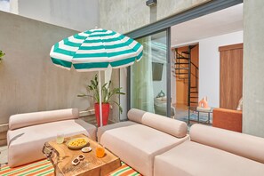 A modern outdoor seating area with a striped umbrella, cushioned sofas, a wooden coffee table with snacks and drinks, and a potted plant. - Stayhere Casablanca - Gauthier Collection (Casablanca)