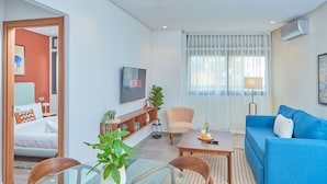 Una sala de estar moderna con un sofá azul, una mesa de centro de madera, una mesa de comedor de vidrio y un televisor en la pared.