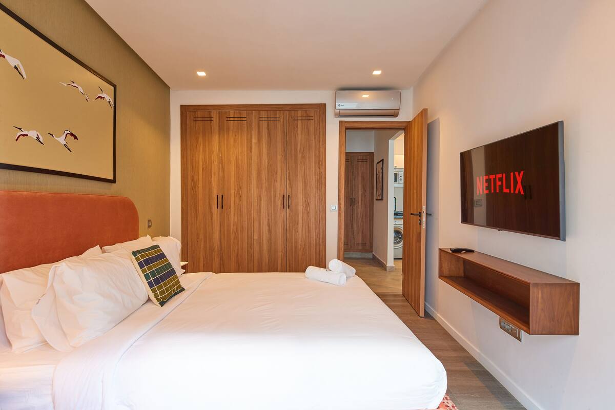 A hotel room with a large bed, wooden wardrobe, a TV mounted on the wall, and a painting on the wall.