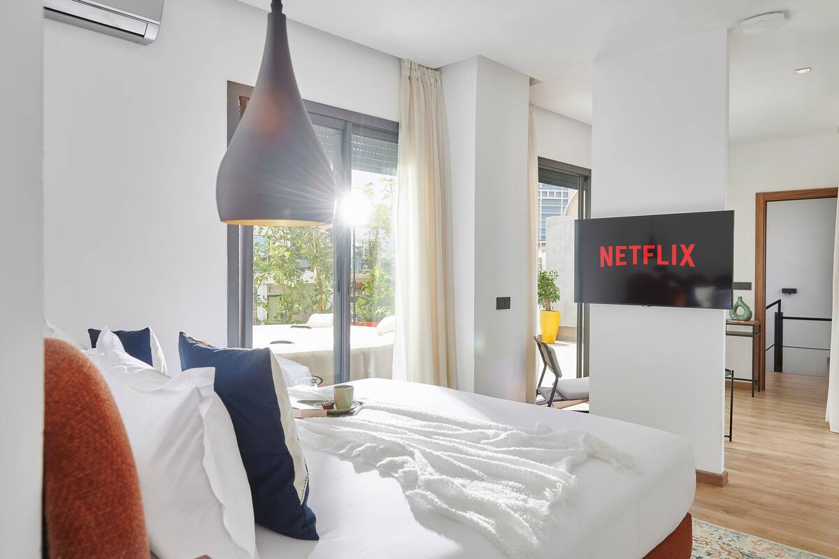 A hotel room with a bed, a TV, a desk, and a window with curtains.