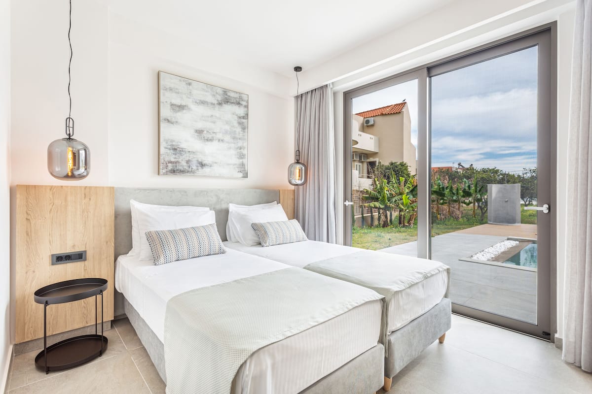 A modern hotel room with two beds, a large window, and a view of the outdoors.