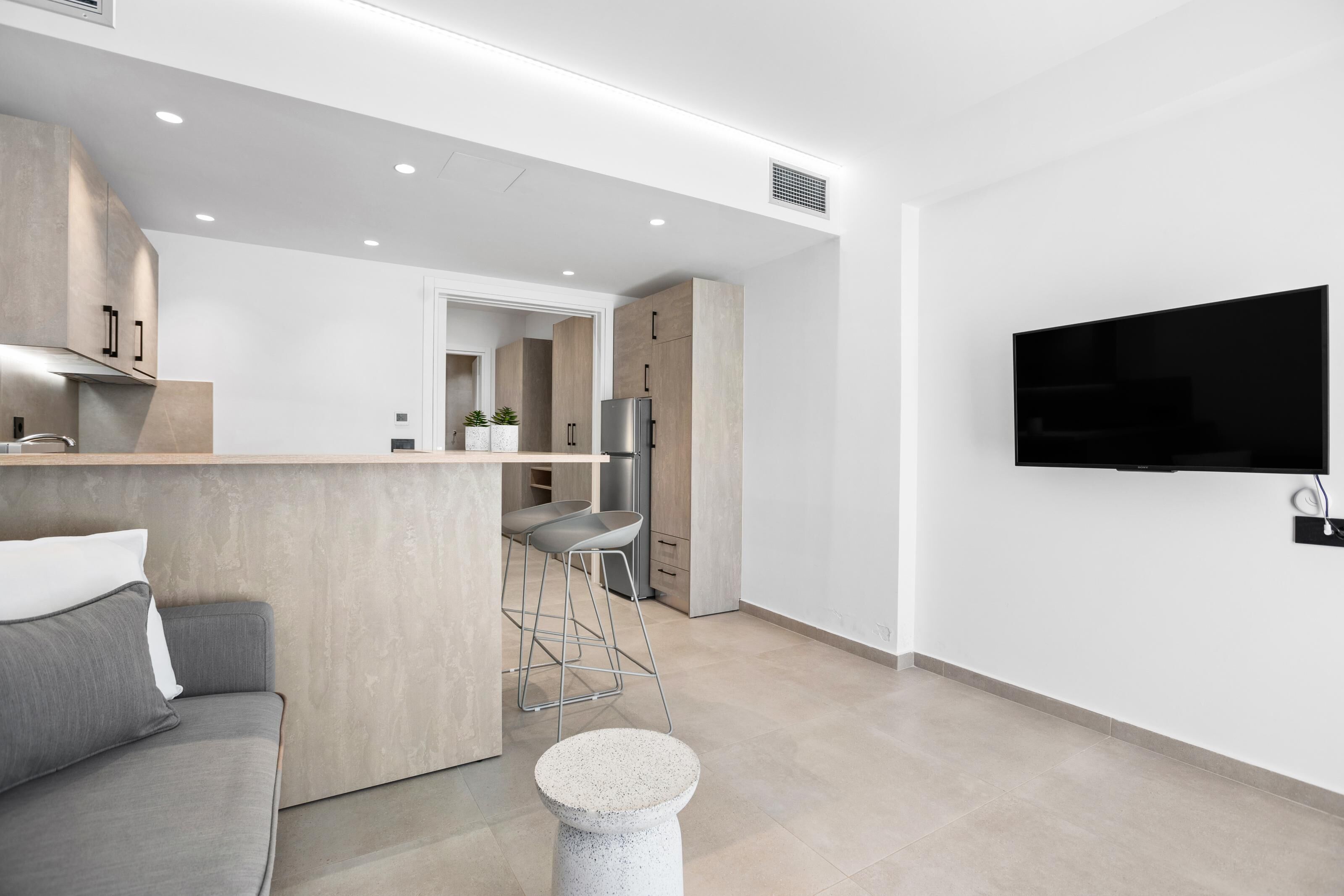 A modern kitchen with a built-in fridge, a bar area, and a seating space with a sofa and stools.