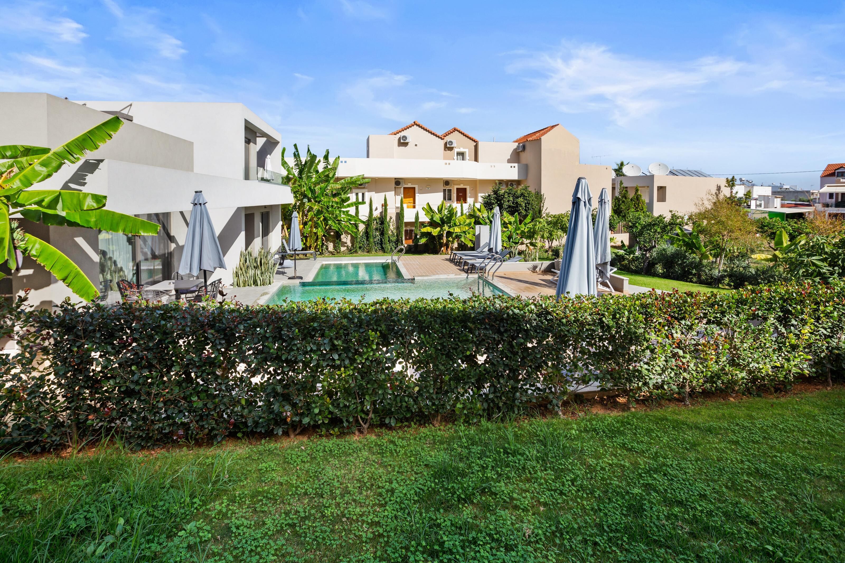A modern hotel with a swimming pool, lounge chairs, and a well-maintained garden.