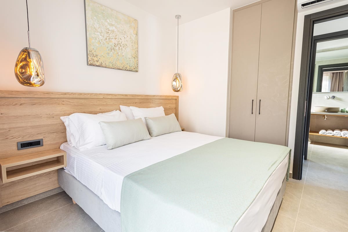 A modern bedroom with a wooden headboard, a bed with white bedding, a bedside table, and a hanging pendant light.