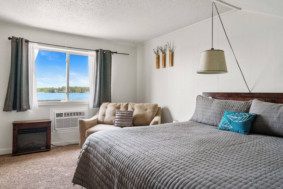 Une chambre avec un grand lit, une chaise, un radiateur et une fenêtre avec des rideaux.