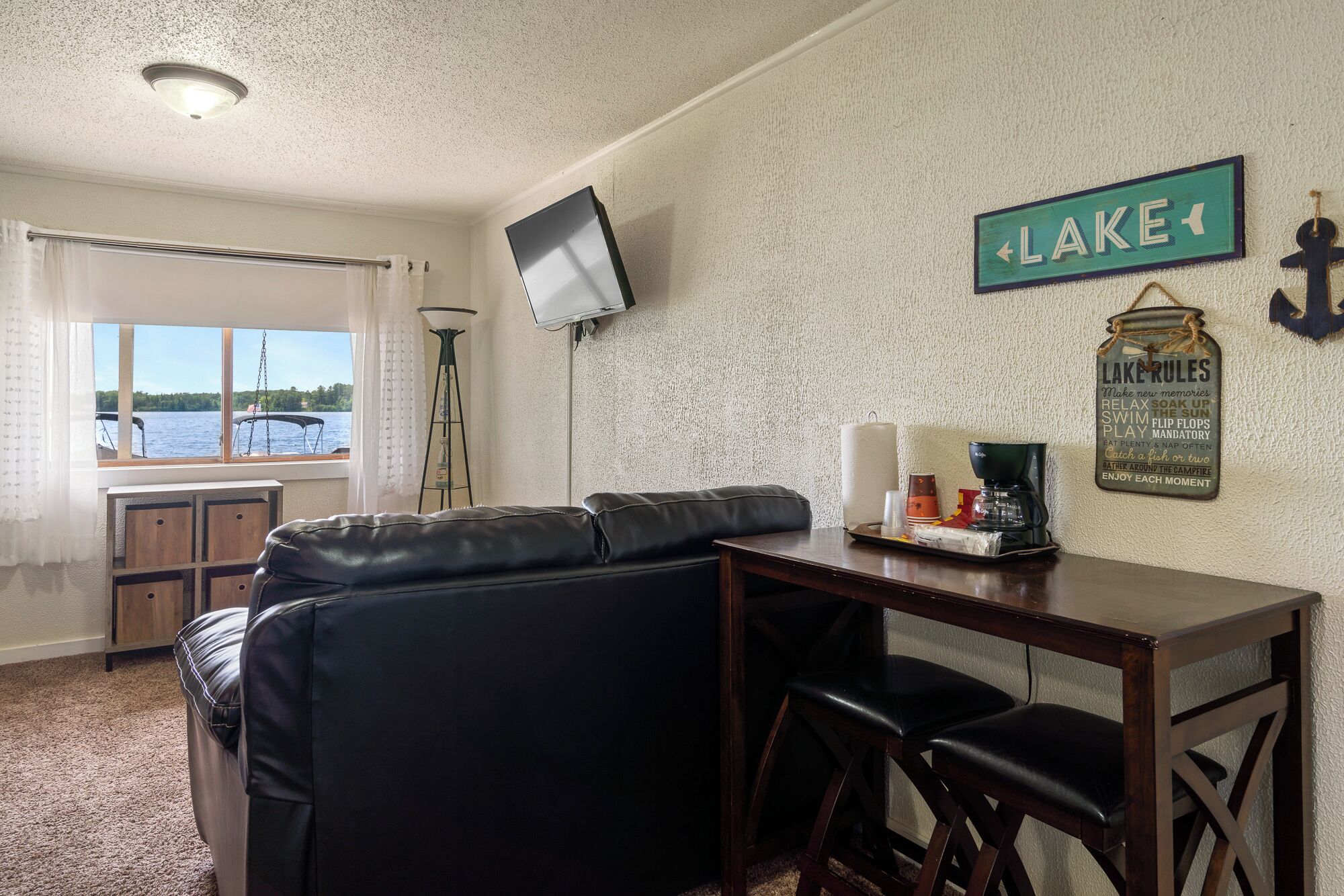 A cozy room with a view of a lake, a television mounted on the wall, a sign reading "LAKE", and a sign with "LAKE RULES".