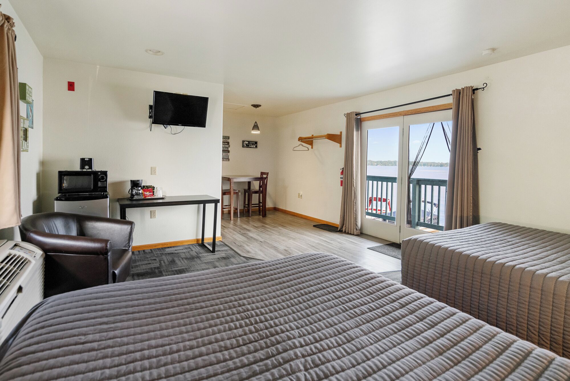 Habitación de hotel con dos camas, un escritorio con televisor, una silla y un balcón con vistas.
