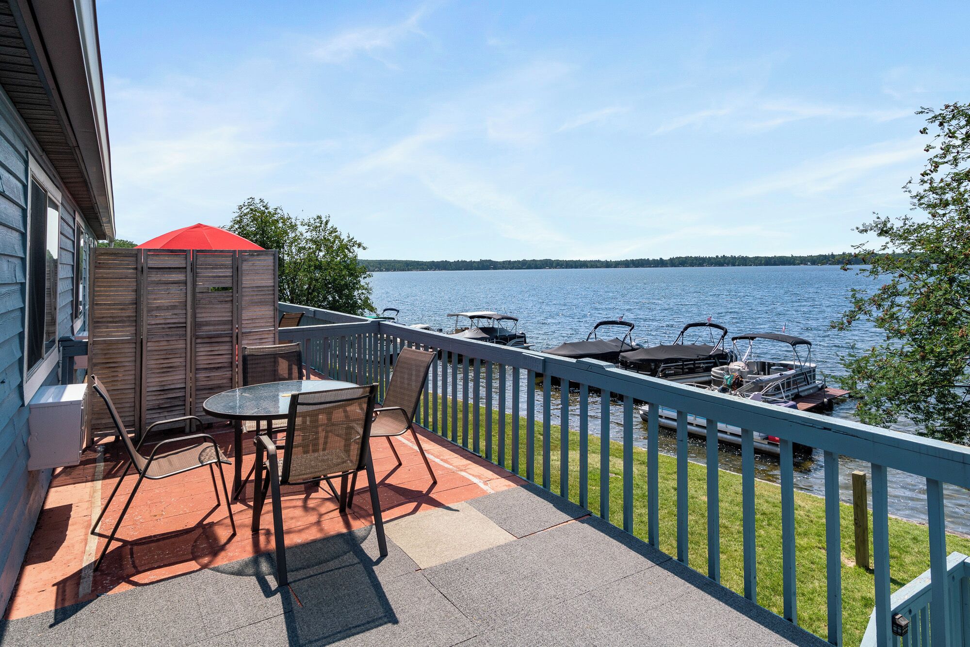 Een balkon met een tafel en stoelen, met uitzicht op een meer met boten.