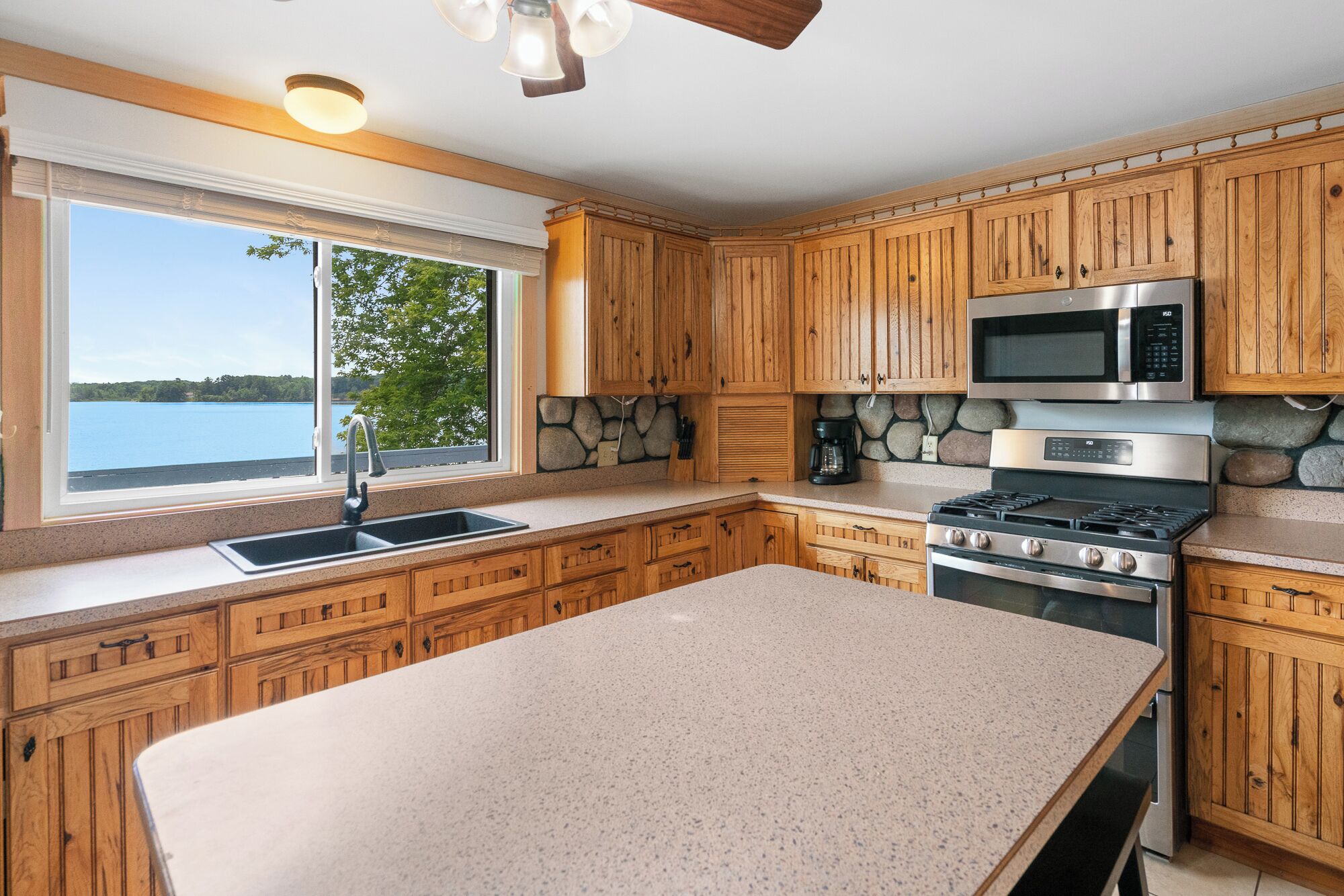 Una cocina con armarios de madera, encimera de granito, estufa, microondas y ventana con vistas a un lago.
