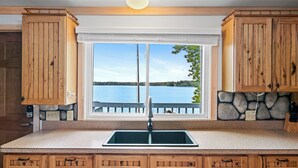 Una cocina con armarios de madera, salpicadero de piedra, un ventanal con vistas a un lago y un lavabo empotrado.