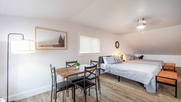 Een slaapkamer met een bed, nachtkastjes, een bureau met stoelen, een vloerlamp en een schilderij aan de muur.