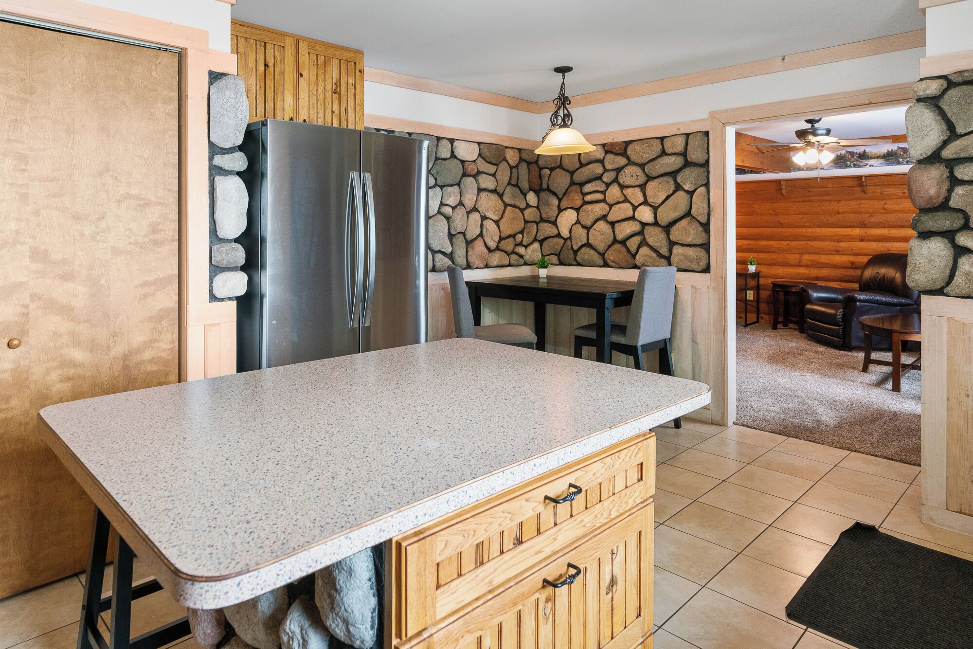 Une cuisine dotée d’un plan de travail en granit, de meubles en bois, d’un mur en pierre et d’un coin repas avec une table et des chaises.
