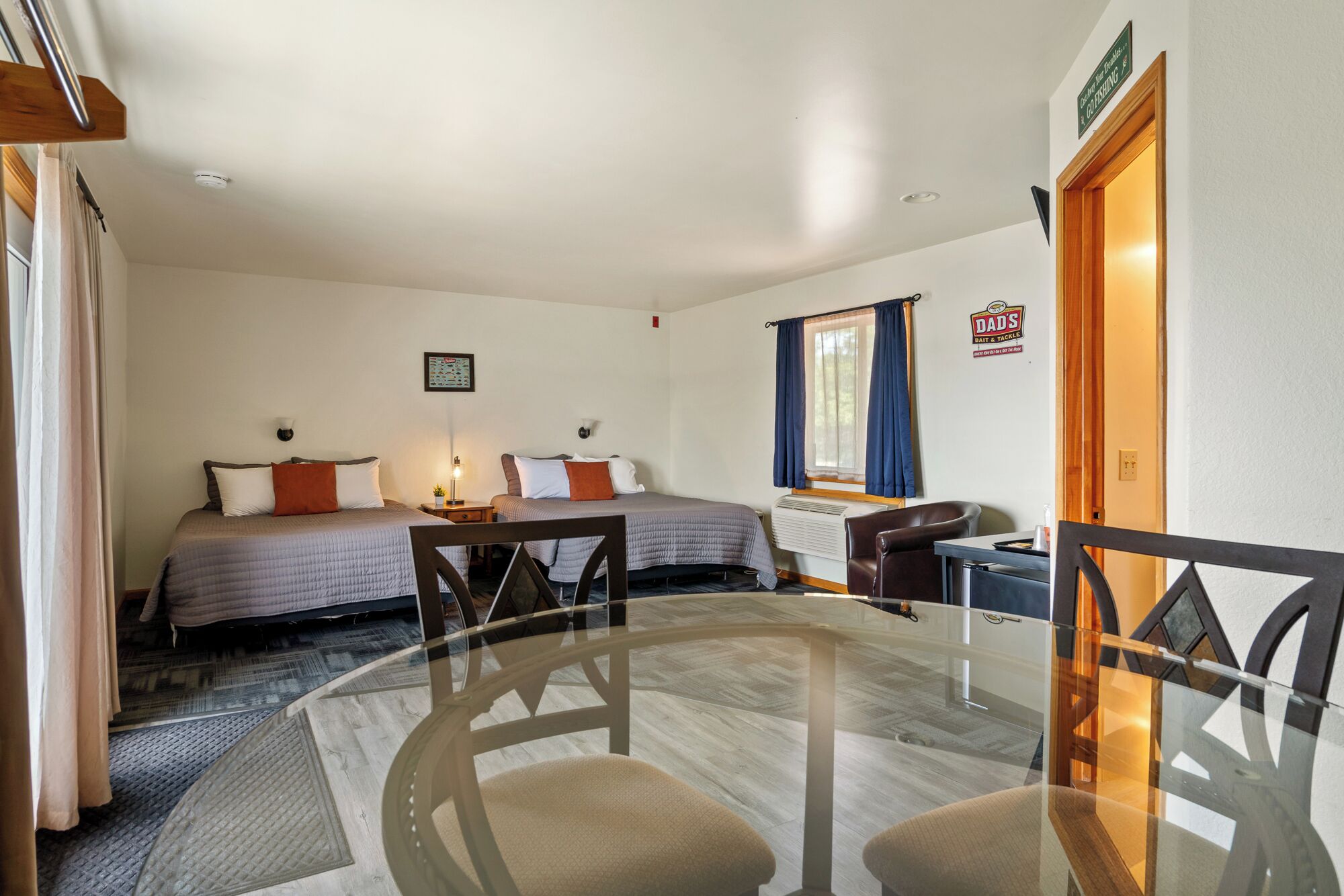 A hotel room with two beds, a dining table, and a small kitchen area.