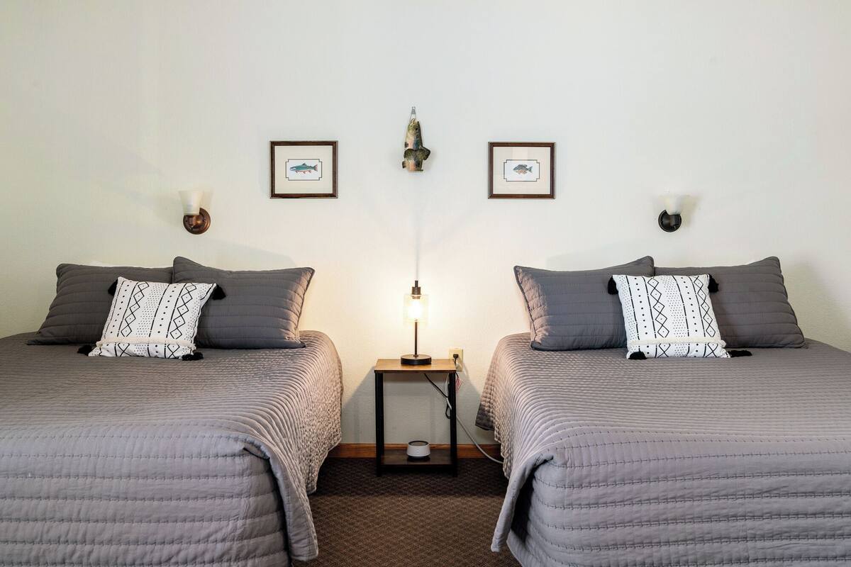 Une chambre avec deux lits, chacun agrémenté d’un oreiller à motifs et d’une tête de lit. Des lampes murales et des tableaux encadrés sont disposés au-dessus des lits.