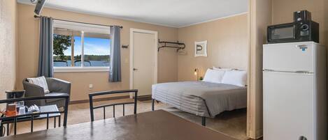 Habitación de hotel con cama, mesa de comedor, una silla, refrigerador, microondas, ventana con vista a un lago e iluminación en el techo.