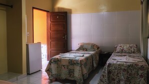 Ein Zimmer mit zwei Betten, einem Kühlschrank und einer Tür zu einem weiteren Raum.