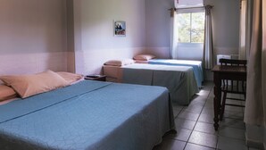 Ein Zimmer mit zwei Betten, einem kleinen Tisch und einem Fenster mit Vorhängen.