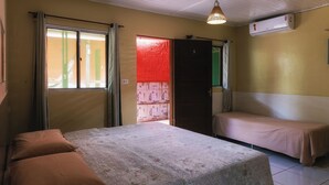 Ein Zimmer mit einem Bett, zwei Einzelbetten, einem Fenster, einer Klimaanlage und einer Tür.