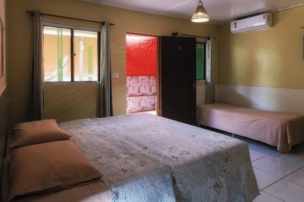 Une chambre comprenant un lit, deux lits simples, une fenêtre, un climatiseur et une porte.