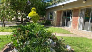 Un edificio con fachada de ladrillo, amplios ventanales y un jardín bien cuidado con diversas plantas y una escultura vegetal.