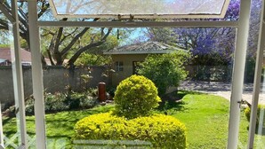 A conservatory with a view of a well-maintained garden, a house in the background, and a clear sky.