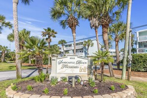 A sign for Sandcastle Beach Townhomes with a clear view of the surrounding palm trees and a road in the background.