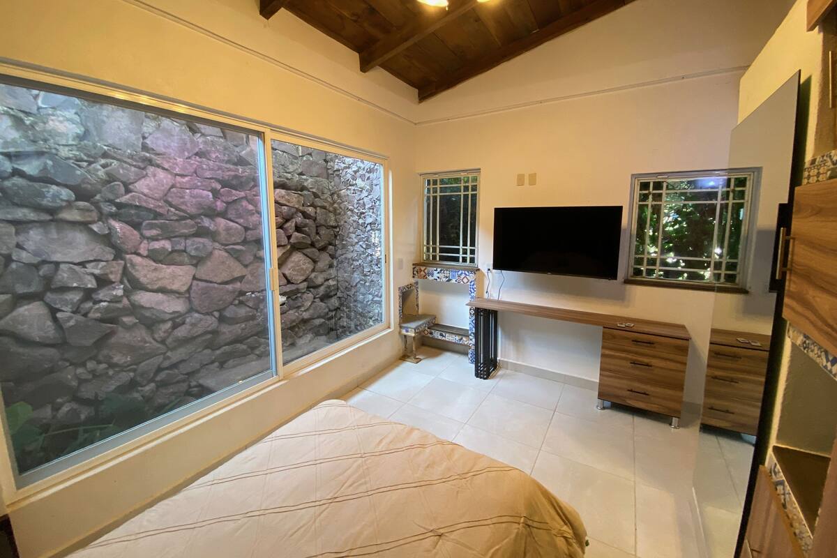 Une chambre avec un lit, une télévision, un bureau et un mur en pierre.