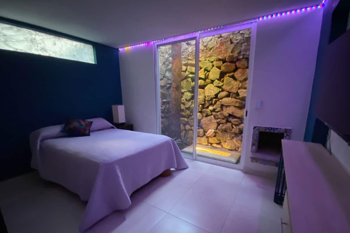 Une chambre à coucher avec un lit, une table de chevet, une cheminée et un mur en pierre.