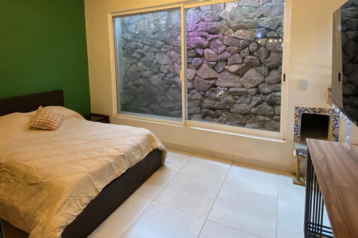 Une chambre à coucher avec un lit, un mur en pierre, une fenêtre et un plafond en bois.