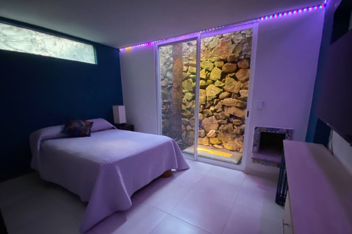 Une chambre à coucher avec un lit, une table de chevet, une cheminée et un mur en pierre.
