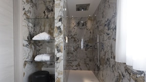 A modern bathroom with marble walls, a glass shelf with towels, a black trash bin, and a shower area. - Agriturismo Redó (Ponti sul Mincio)