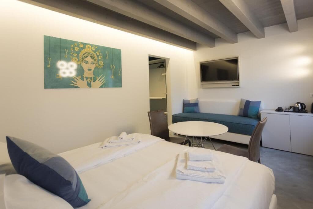 Ein Hotelzimmer mit einem Bett, einem kleinen runden Tisch, einer Couch, einem Fernseher und einem Bild an der Wand.