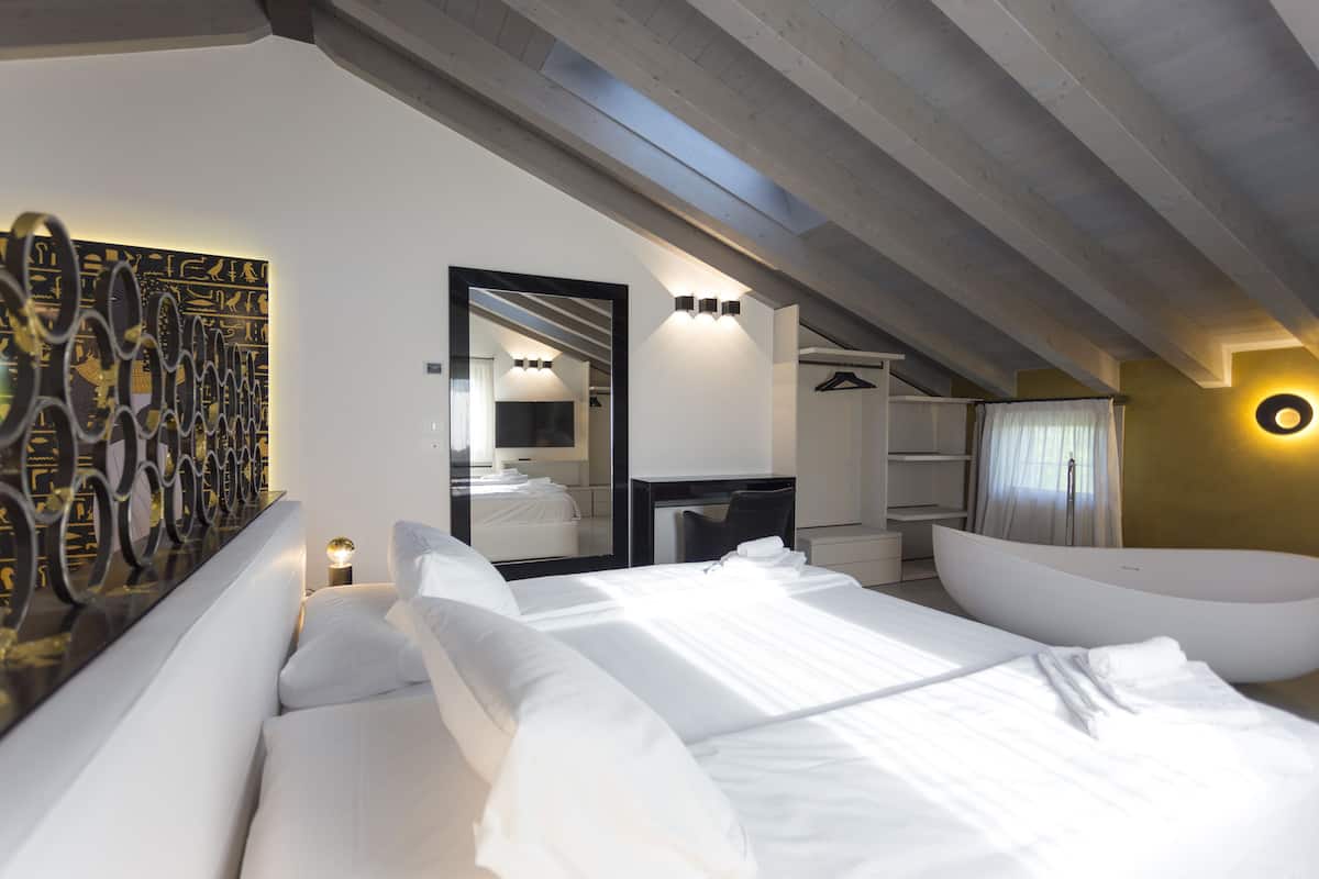 Une chambre d’hôtel moderne avec un grand lit, une baignoire, un miroir et un mur orné de motifs décoratifs.